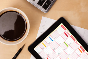 Workplace with tablet pc showing calendar and a cup of coffee on